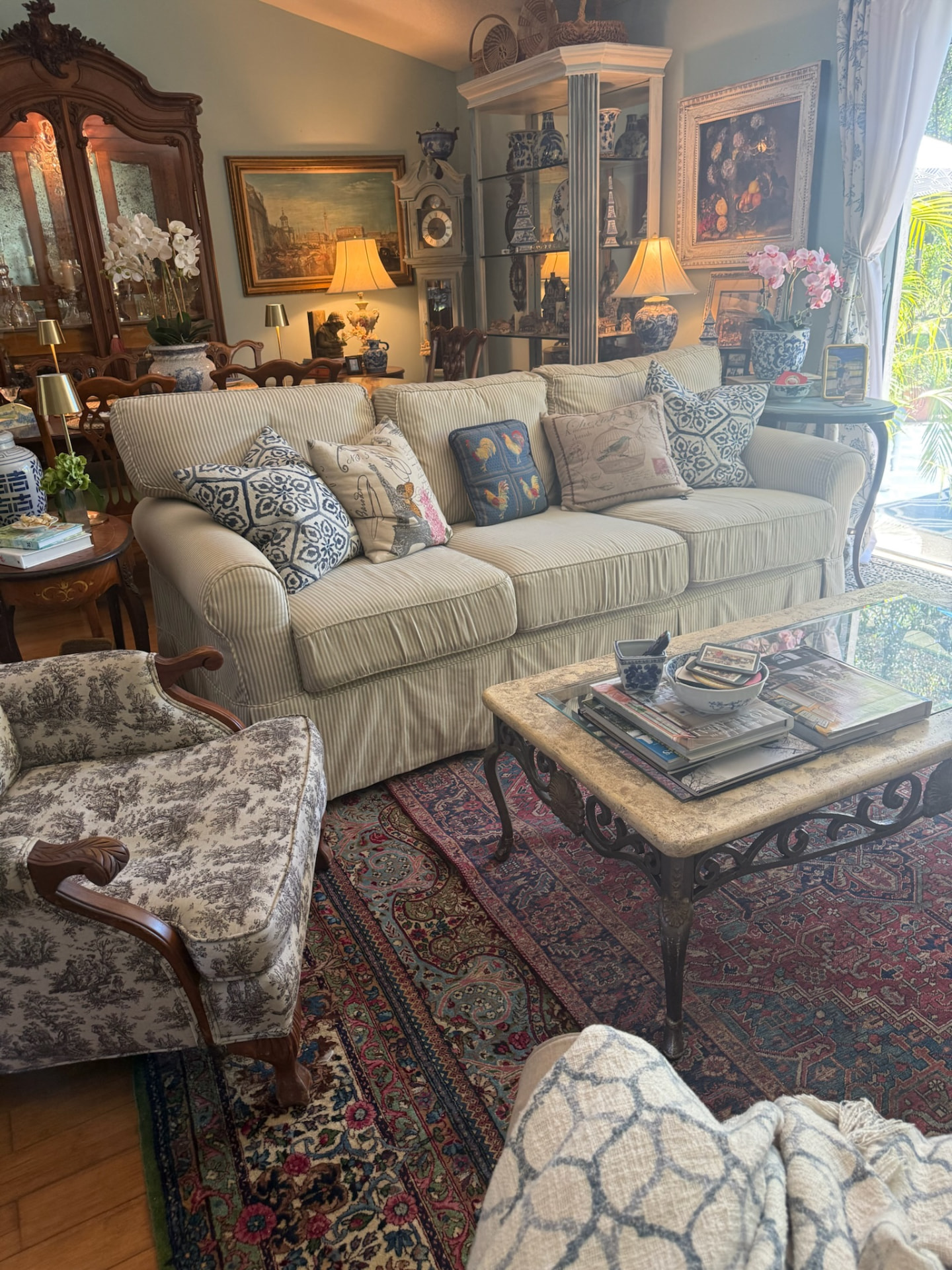 Collected Southern living room with a ticking-stripe sofa, toile armchair, antique armoire and layered Persian rugs